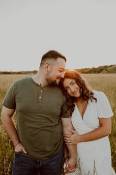 a man and woman are standing in the middle of a field with tall grass at sunset