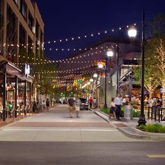 people are walking down the street in front of shops and restaurants at night with lights strung over them