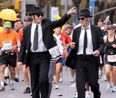 two men in suits and ties are walking down the street with other people behind them