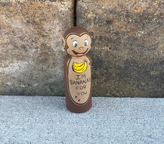 a wooden monkey with a banana for you sign on it's back sitting next to a stone wall