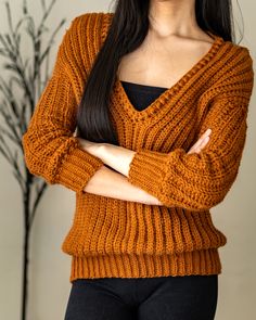 a woman with her arms crossed wearing an orange sweater