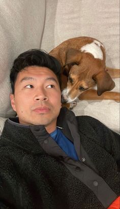 a man laying on top of a couch next to a brown and white dog in his lap