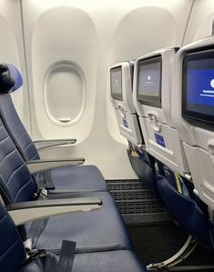 the inside of an airplane with blue leather seats and flat screen tv on the wall