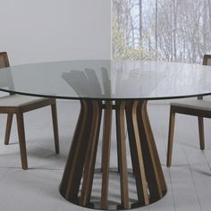 a round glass table with wooden chairs around it and a white wall in the background