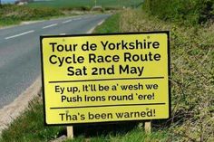 a yellow sign sitting on the side of a road next to a lush green field