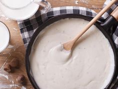 a pan filled with white sauce and wooden spoons on top of a checkered cloth