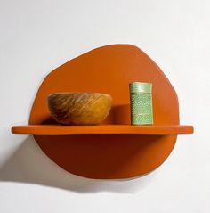 an orange shelf with a wooden bowl on it and a green cup sitting on top