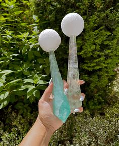 a hand holding two glass vases in front of some bushes