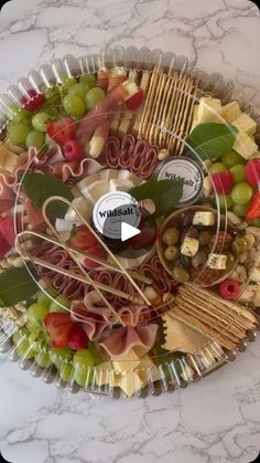 a platter filled with lots of different types of cheeses and vegetables on top of a marble counter