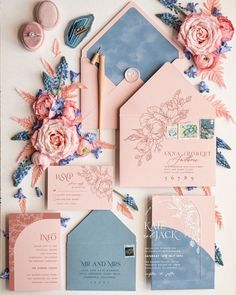 the wedding stationery is laid out on top of each other with pink flowers and blue envelopes