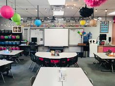 an empty classroom with tables and chairs in front of a whiteboard, balloons and other decorations hanging from the ceiling