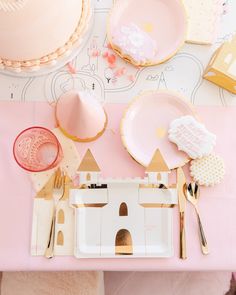 a pink table topped with plates and utensils next to a castle shaped cake