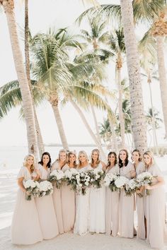 a group of women standing next to each other in front of palm trees on the beach