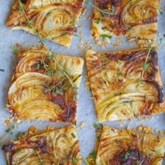 several square pieces of food sitting on top of a sheet of baking paper with herbs