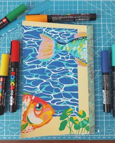 some markers and pens are laying on top of a piece of paper with an image of a fish