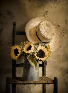 sunflowers in a vase with a straw hat on the back of a chair