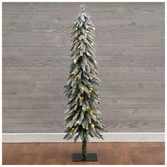 a white christmas tree with lights on it in front of a wooden wall and floor