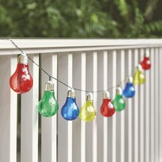 multicolored light bulbs are hanging on a white fence