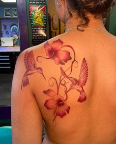 the back of a woman's shoulder with hummingbirds and flowers tattoo on it