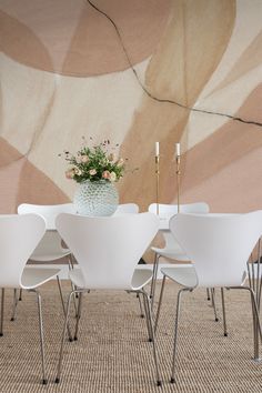 a dining room table with white chairs and a vase on top of it in front of a wall mural