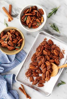 two bowls filled with pecans on top of a white counter next to cinnamon sticks