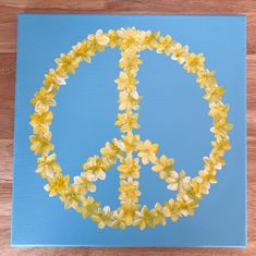 a peace sign made out of yellow flowers on a blue background with wood flooring