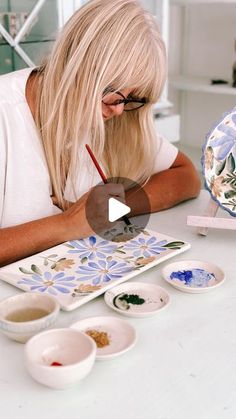 a woman is painting on a table with bowls and plates in front of her,