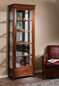 a brown leather chair sitting next to a tall wooden case with glass doors on it