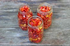 four mason jars filled with red and yellow peppers on top of a wooden table,