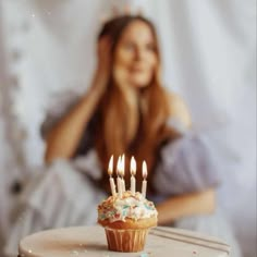 a cupcake with lit candles sitting on top of a table next to a woman