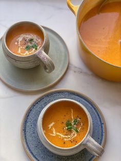 two bowls of soup are sitting on plates next to a pot and saucer,