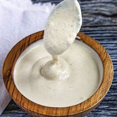 a wooden bowl filled with white sauce and a spoon sticking out of the dip in it