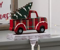 a red truck with a christmas tree in the back sits on a shelf next to a sign that says merry christmas