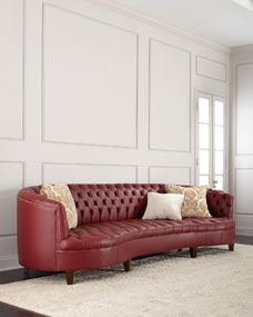 a red leather couch sitting on top of a rug in front of a white wall