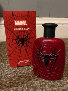 a spider man cologne bottle next to a red box on the ground with a black spider - man sticker