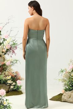 a woman standing in front of flowers wearing a long green dress with one shoulder open