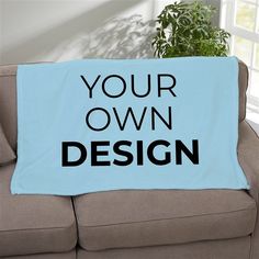 a couch with a blue blanket that says your own design on it and a potted plant in the corner