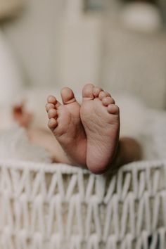 a baby's bare feet laying on top of a white blanket in a basket