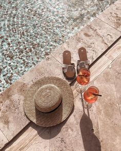 a straw hat and two glasses of wine next to an empty swimming pool with flip flops on the floor