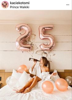 a woman laying on top of a bed in front of balloons and number twenty five