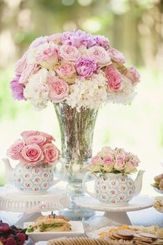 a vase filled with pink roses sitting on top of a table next to plates and cups