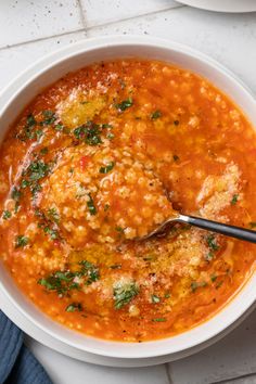 a bowl of soup with meatballs and parsley in it on a white table