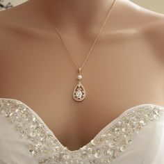 the back of a woman's wedding dress with a necklace on her shoulder and a diamond pendant hanging from it