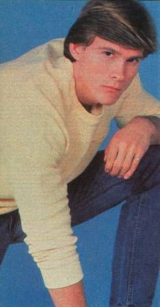 the young man is posing for a photo in jeans and a sweater with his hands on his knees