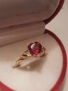 a ring with a red stone in it sitting on top of a white cloth covered box