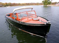 an orange and black boat floating on top of a lake next to a shore line