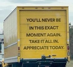 a yellow truck driving down a road next to a white truck with a message on the back