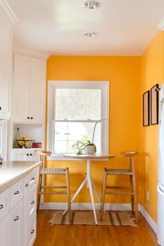 two chairs sitting at a table in front of a window with yellow walls and white cabinets