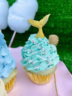 there are two cupcakes with blue frosting and a mermaid tail on top