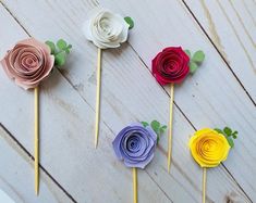 four paper flowers on sticks with leaves and stems in different colors, sitting on a wooden surface